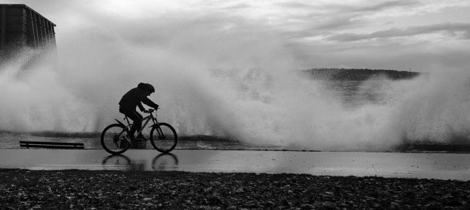 A person biking along the seawall with big waves in the background A person biking along the seawall with big waves in the background