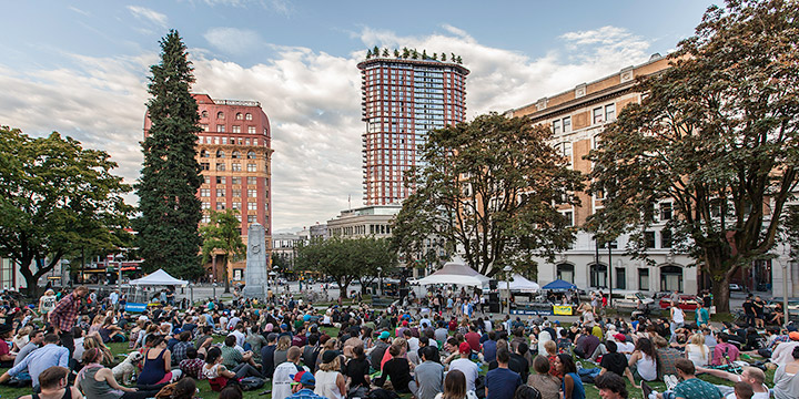 People gathered at Victory Square to watch a music concert, with heritage buildings along Hastings Street in the background People gathered at Victory Square to watch a music concert, with heritage buildings along Hastings Street in the background