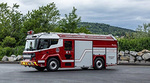An electric fire truck parked with bushes and rocks in the background An electric fire truck parked with bushes and rocks in the background